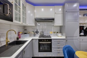 A compact kitchen with a built-in oven, a gas stove, and a microwave. There are cabinets with handles, a sink, and a kettle on the countertop. - AzureGold Apartment (Senglea)