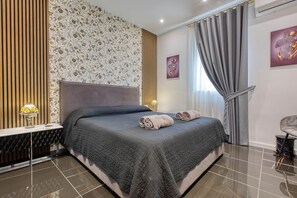 A modern bedroom with a large bed, a headboard, a patterned wall, a window with curtains, and a lamp. - AzureGold Apartment (Senglea)