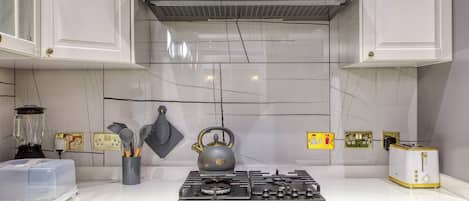 A kitchen with white cabinets, a gas stove, a kettle, and a toaster.