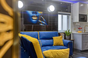A modern living room with a blue sofa, a yellow pillow, and a large TV screen displaying a close-up image. - AzureGold Apartment (Senglea)