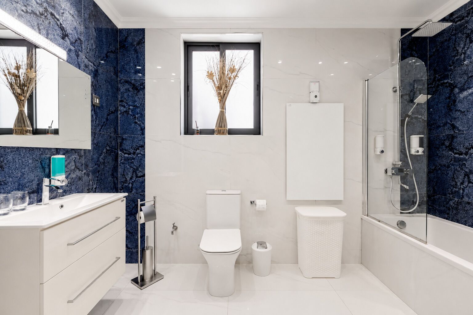 Un bagno moderno con schienale in marmo, un WC, un lavabo con specchio, una doccia e una finestra con vista sugli alberi.