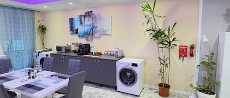 A modern kitchen with a washing machine, dining table, chairs, and a potted plant.
