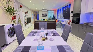 A modern dining area with a table set for four, a washing machine, a sofa, and a Christmas tree. - Azure Apartment (Senglea)