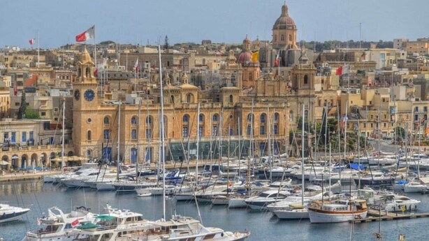 A marina with numerous boats docked, a prominent building with a dome and clock tower, and a densely packed urban backdrop. - Azure Apartment (Senglea)