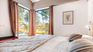 A bedroom with a large bed, a piano, and a view of an outdoor area with a table and chairs.