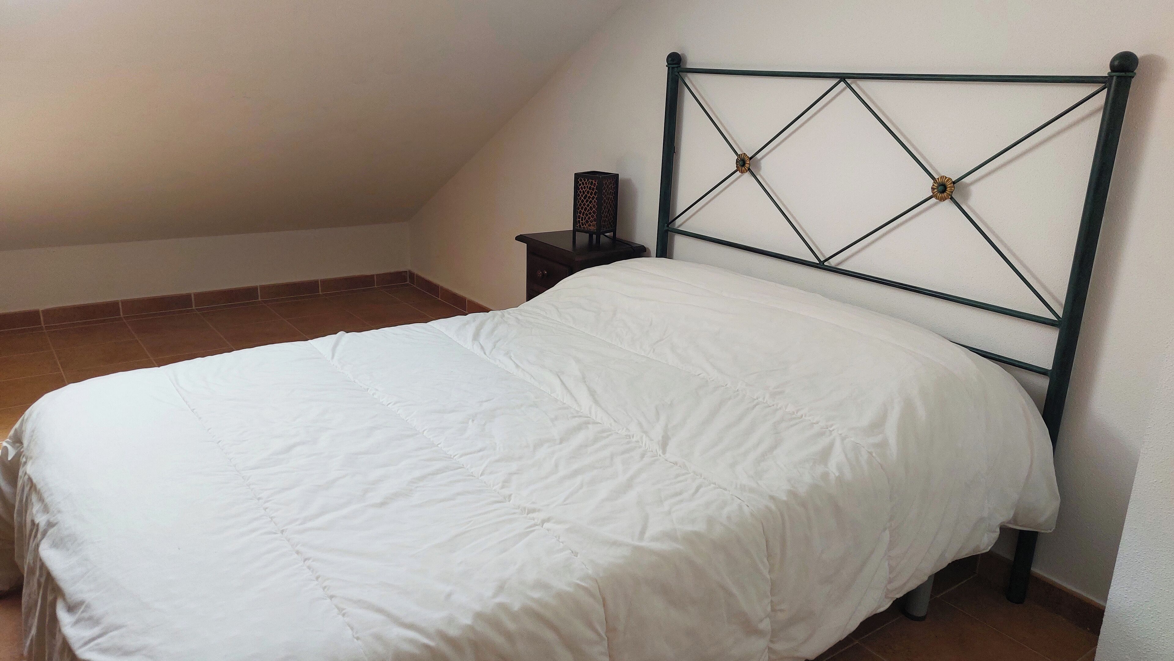 A single bed with a white duvet in a room with a sloped ceiling and tiled floor.
