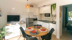 A modern kitchen with white cabinets, a microwave, and a refrigerator. There is a dining table with black chairs and red placemats. - WELCS APARTMENT 295 EMP with community pool (Rosas / Roses)