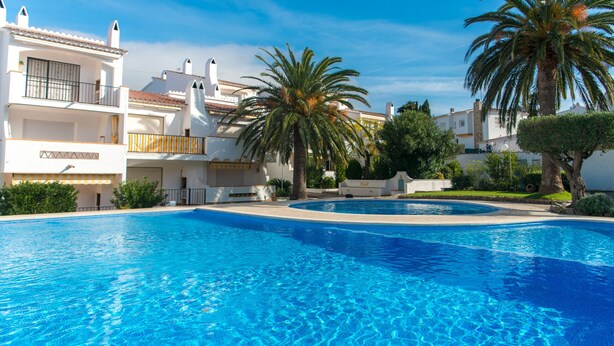 A swimming pool with clear blue water, surrounded by white buildings with balconies and palm trees. - WELCS APARTMENT 295 EMP with community pool (Rosas / Roses)