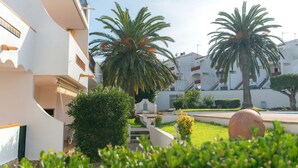 A courtyard with palm trees, a large decorative stone, and a white building with balconies. - WELCS APARTMENT 295 EMP with community pool (Rosas / Roses)