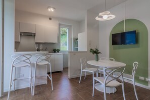 A modern kitchen with white cabinetry, a dining area with white chairs, and a green accent wall.