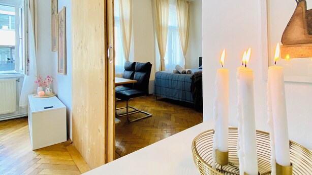 A modern living room with a wooden floor, a white sofa, a small side table with a vase, and a framed picture on the wall. - Cozy 2BR Apartment Near Westbahnhof (Vienna)