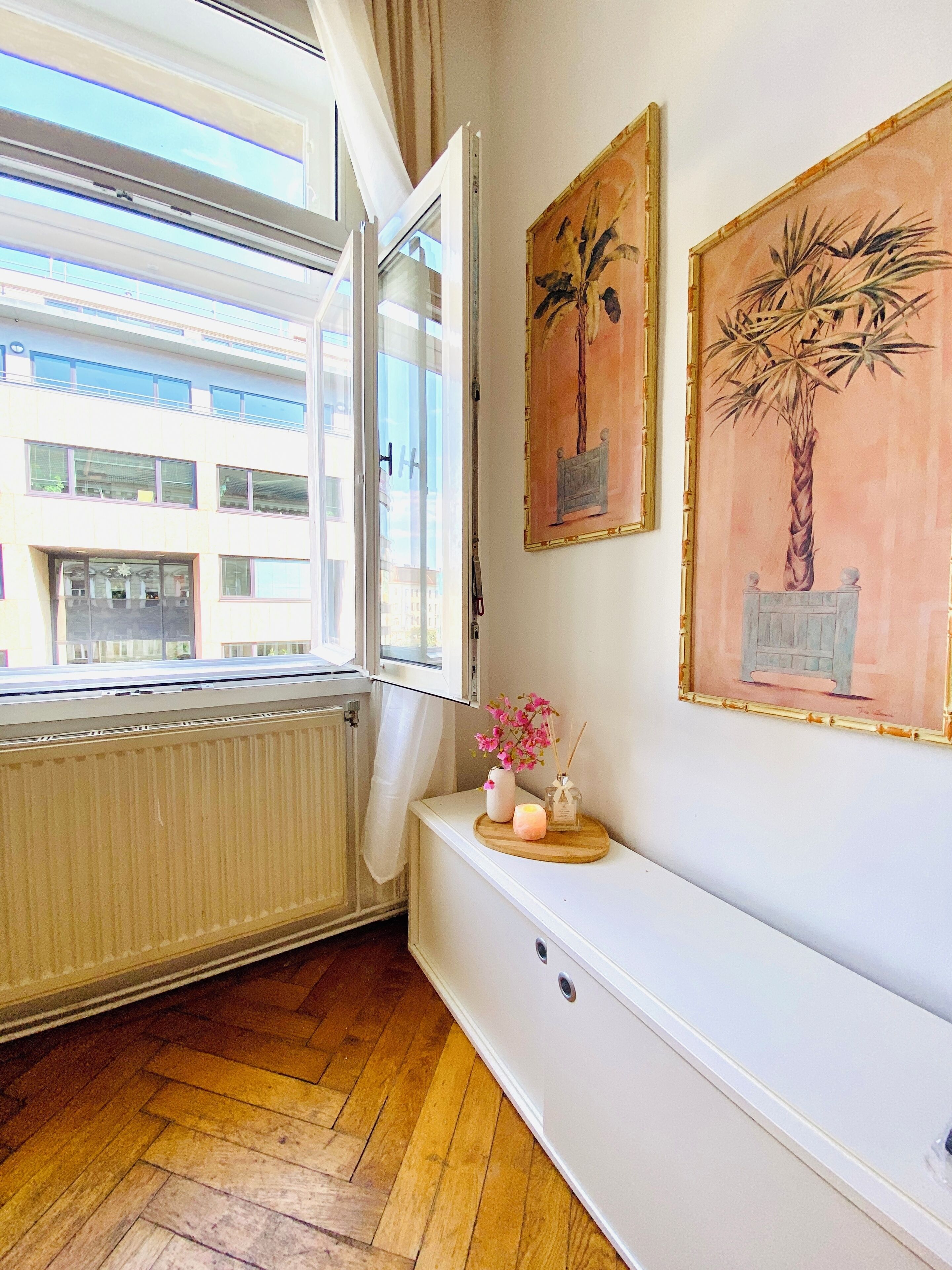 Une pièce avec une fenêtre, un radiateur, un banc et deux tableaux encadrés accrochés au mur.