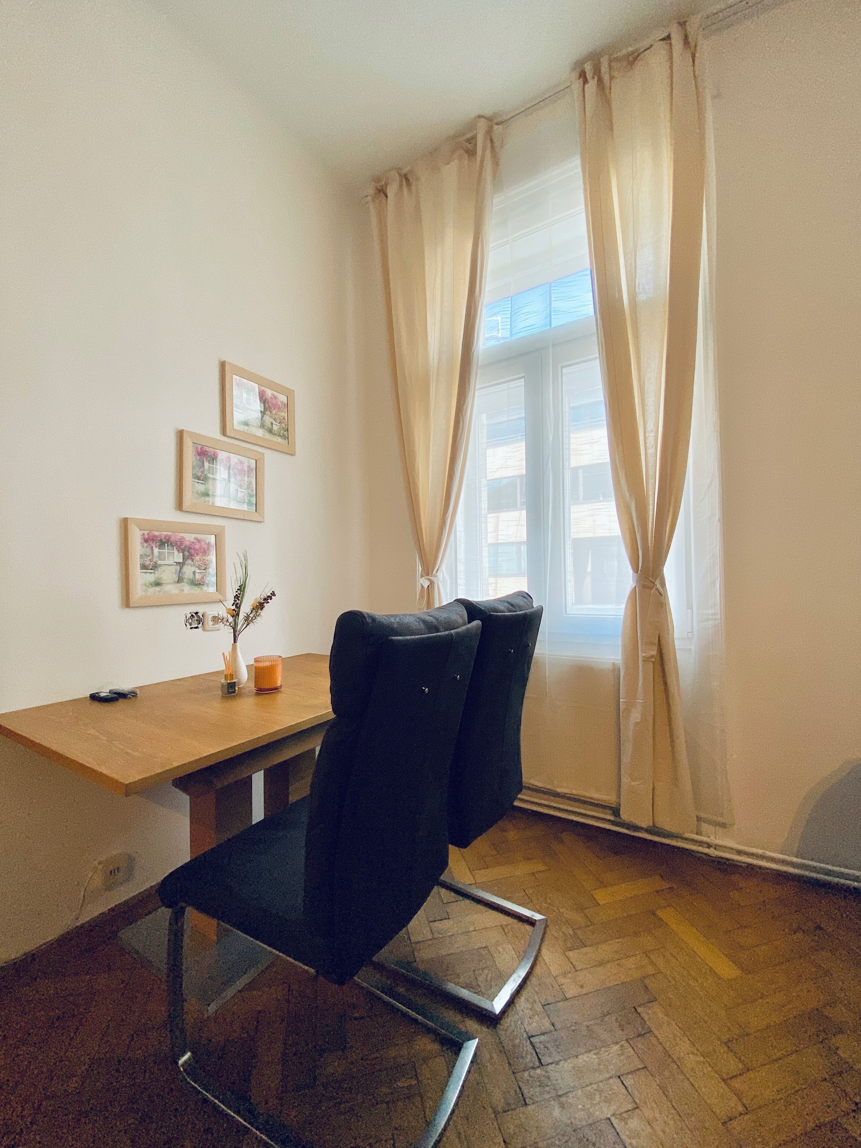 Ein Zimmer mit einem Holztisch, zwei schwarzen Stühlen, einer Blumenvase und drei gerahmten Bildern an der Wand.