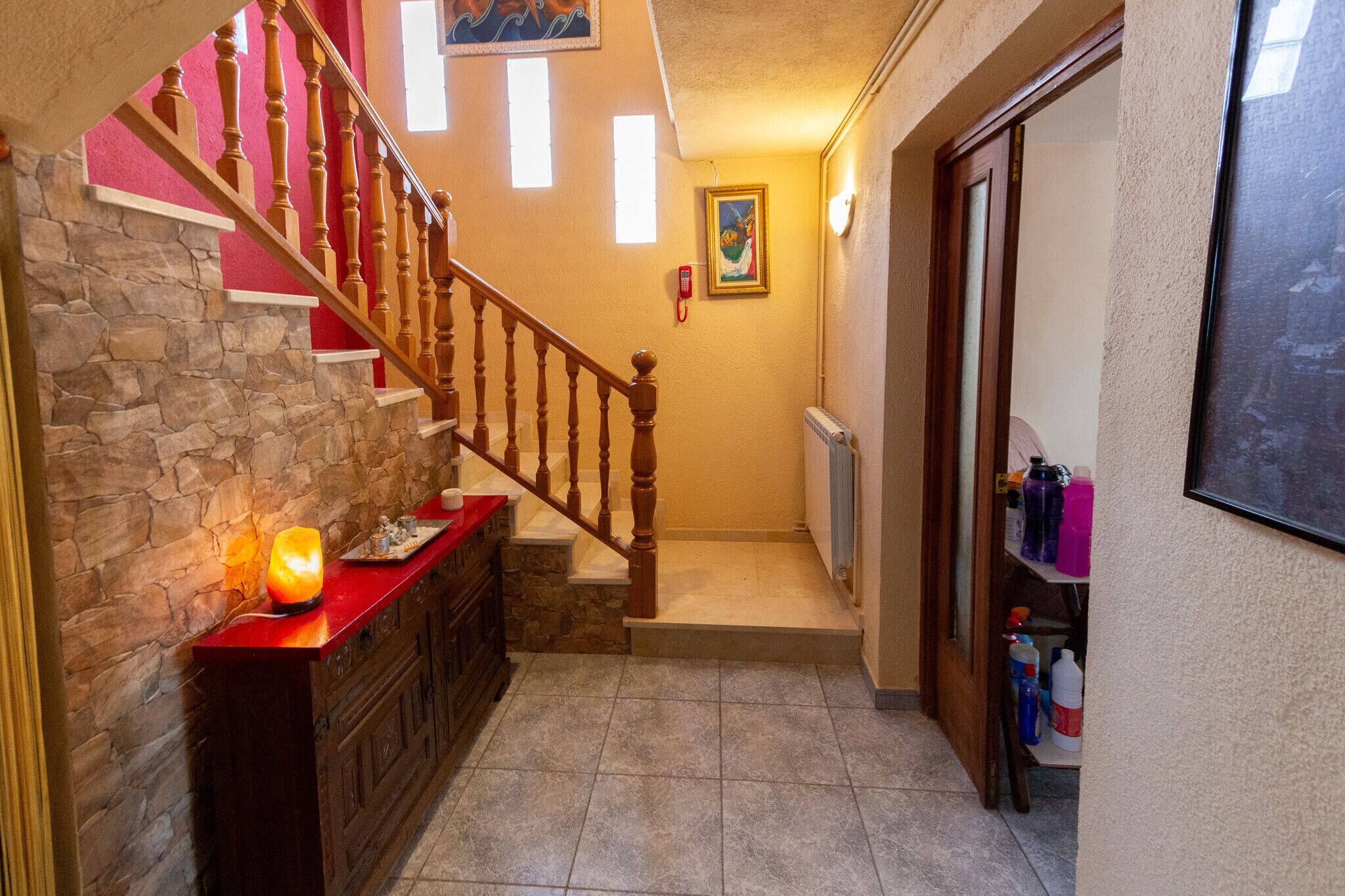 Un escalier avec des balustrades en bois, un mur en pierre et un comptoir rouge sur lequel est posée une bougie.