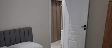 A neatly made bed with white linens and a grey headboard in a room with a wooden wardrobe and a white door.