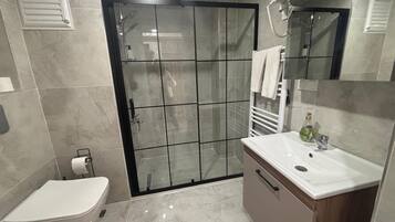 Uma casa de banho moderna com sanita, cabine de duche e toucador com espelho.