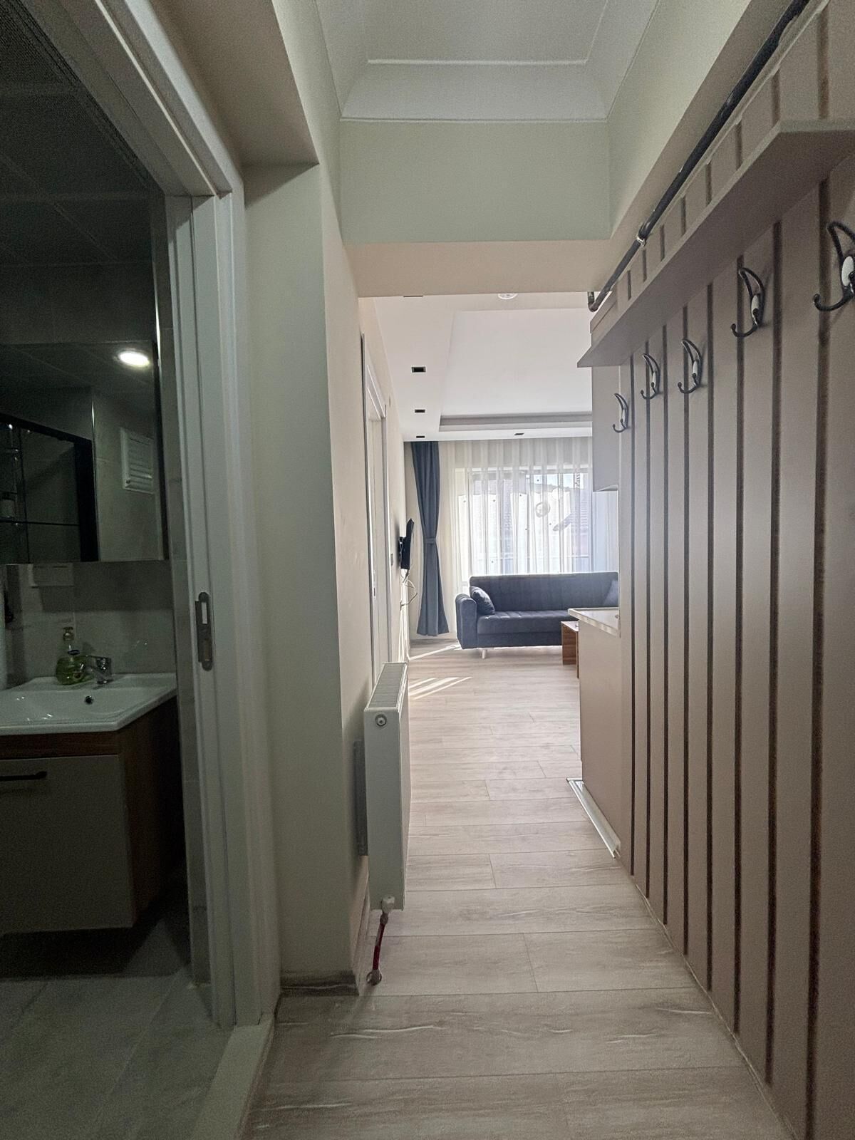 A narrow hallway with a kitchen area on the left, a radiator, and a blue sofa in the distance.
