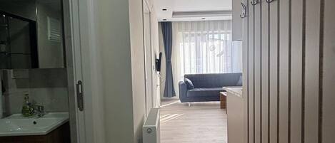 A narrow hallway with a kitchen area on the left, a radiator, and a blue sofa in the distance.