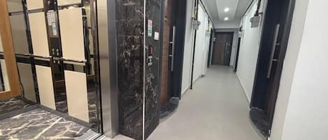 A modern hallway with a marble floor, elevator, and glass doors.