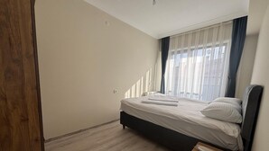 Een slaapkamer met een bed, een houten vloer en een raam met gordijnen.