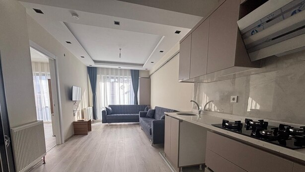 Een moderne keuken met een inbouwfornuis, een spoelbak en een raam met uitzicht op een woonruimte met een bank en gordijnen.