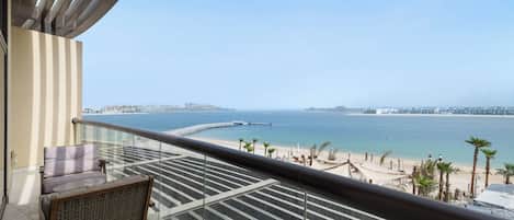 A balcony with a view of the beach and sea, a wicker chair, and a glass railing.