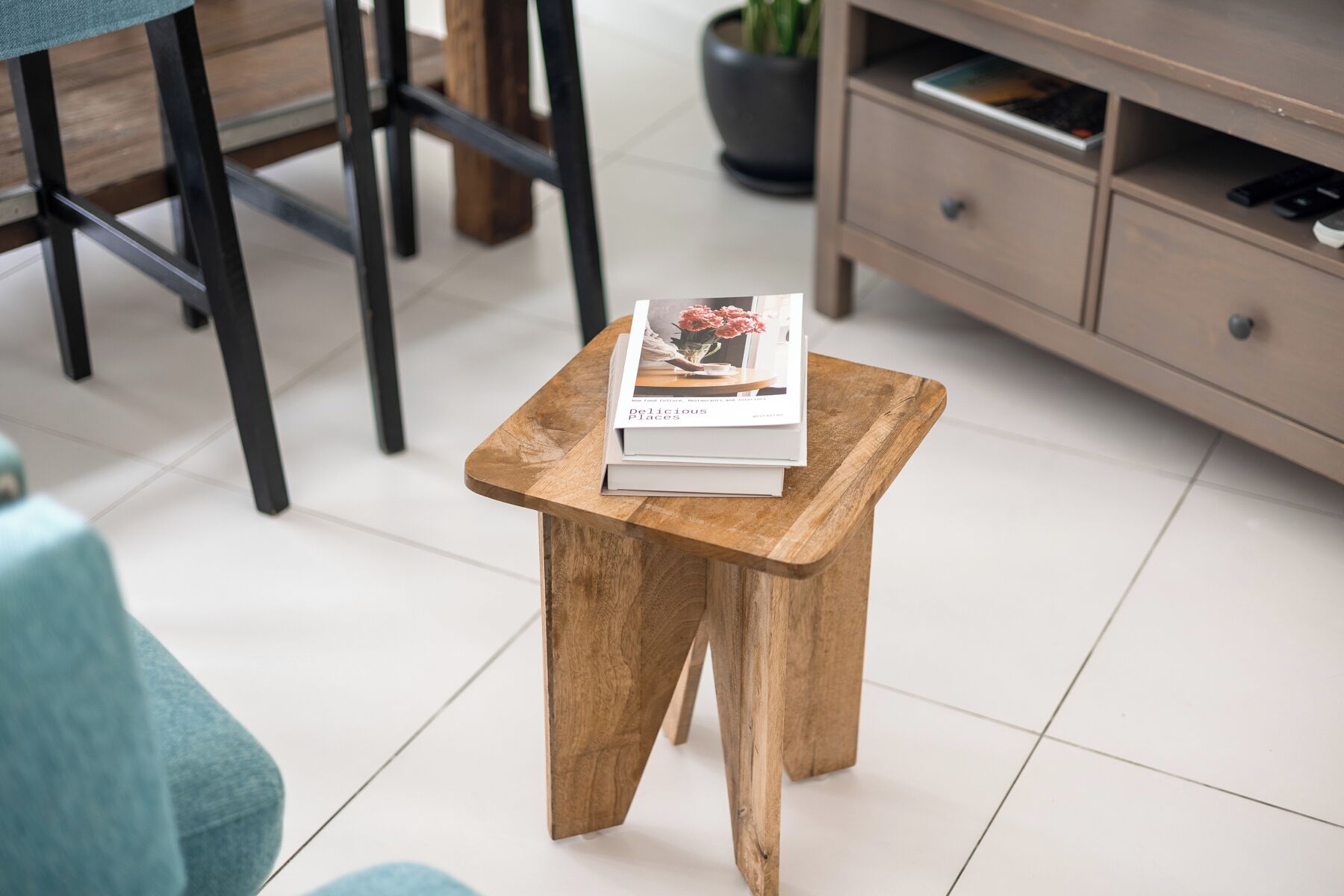 Een klein houten krukje met een boek met de titel 'Delicious Places' erop, staand op een betegelde vloer.