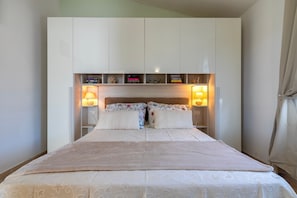 A bedroom with a bed, two bedside lamps, a headboard with shelves, and a bedside table. - Beautiful Penthouse with Sea View (Badesi)