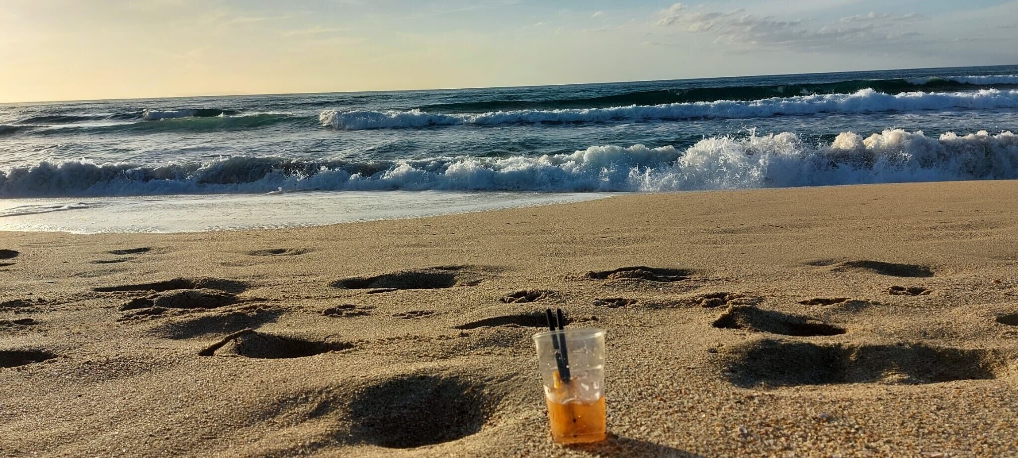 Une plage parsemée d’empreintes et sur laquelle on trouve un gobelet en plastique avec des pailles.