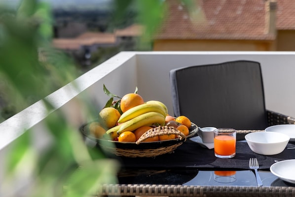 A table with a fruit basket, a glass of orange juice, and dining utensils.
