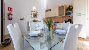 Una cocina moderna con armarios blancos, microondas y un comedor con mesa de vidrio y sillas blancas.