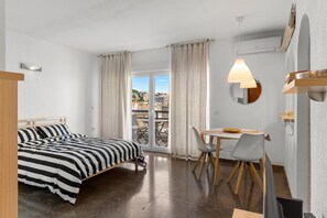 Une chambre à coucher avec un lit, une table à manger avec des chaises, un balcon avec des rideaux et une lampe suspendue.