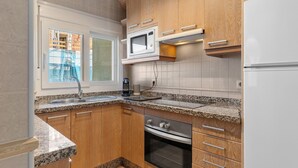 Eine kleine Küche mit Holzausstattung, einer eingebauten Mikrowelle, einem Edelstahlbackofen und einer Arbeitsplatte aus Granit.