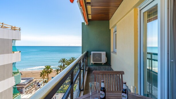 Ein Balkon mit Blick auf den Strand, eine Klimaanlage und ein Tisch mit Flasche und Glas.