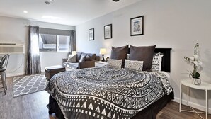 A modern bedroom with a large bed, a ceiling fan, a bedside table, a lamp, and a window with curtains. - Killington Center Renovated Studio with Kitchenette on Bus Route and Discounted Ski Rentals. (Killington)