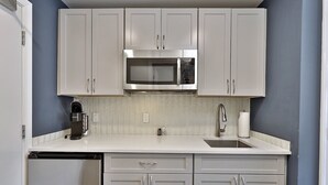 A kitchen with white cabinets, a stainless steel microwave, a coffee maker, and a sink. - Killington Center Renovated Studio with Kitchenette on Bus Route and Discounted Ski Rentals. (Killington)