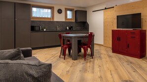 A modern kitchen with a dining area, wooden flooring, and a red cabinet with a TV. - Trento 2 (Bormio)