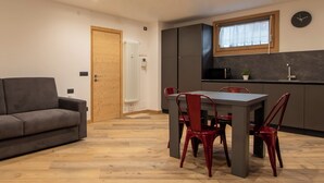 A compact living space with a sofa, dining table, and chairs, a kitchenette with a microwave, and a window with a curtain. - Trento 2 (Bormio)