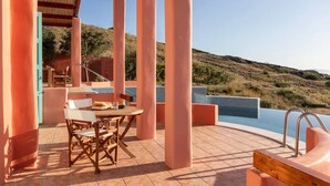 A covered outdoor area with a pool, wooden furniture, and a view of the hills. - Villa Malia, Eco-Chic Villa with SeaViews (Syros)