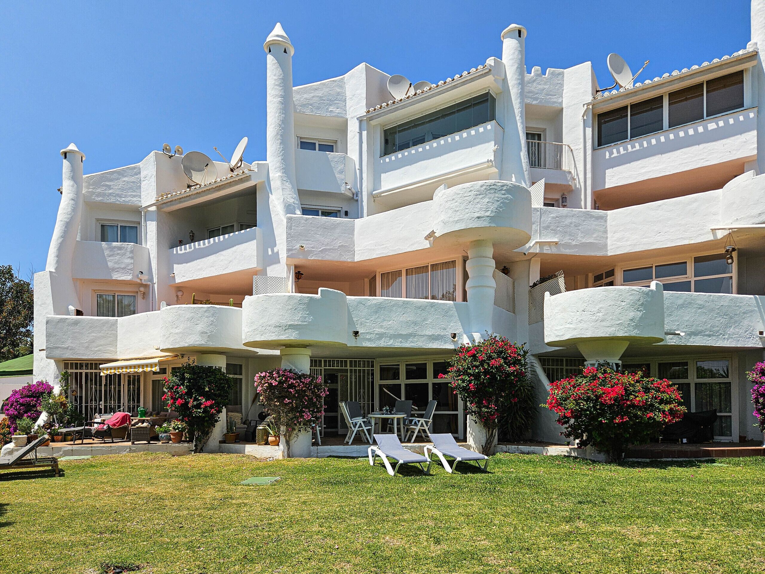 A multi-story building with balconies, outdoor seating, and potted plants.