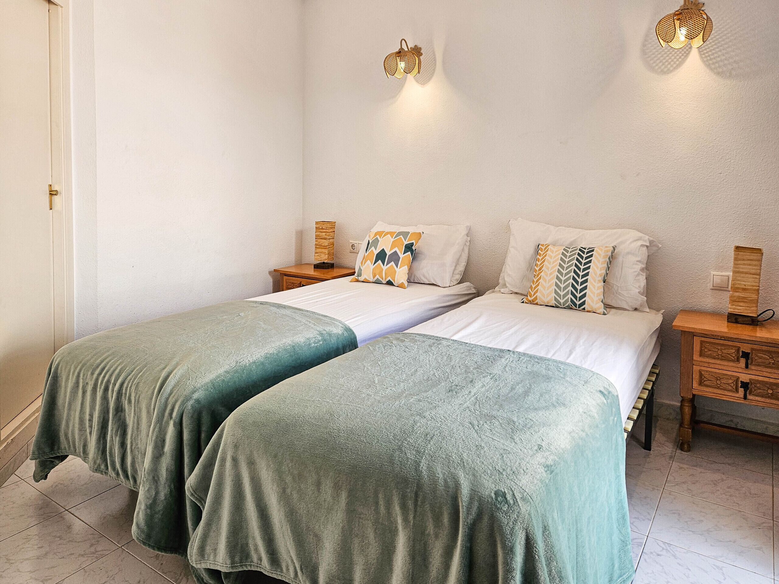 Een tweepersoonsbed met twee nachtkastjes, elk met een lamp, en een houten dressoir met lades.