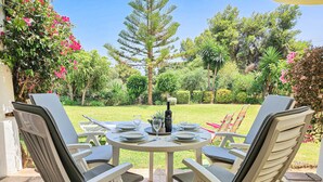 A round table with four chairs, set outdoors with a garden view.