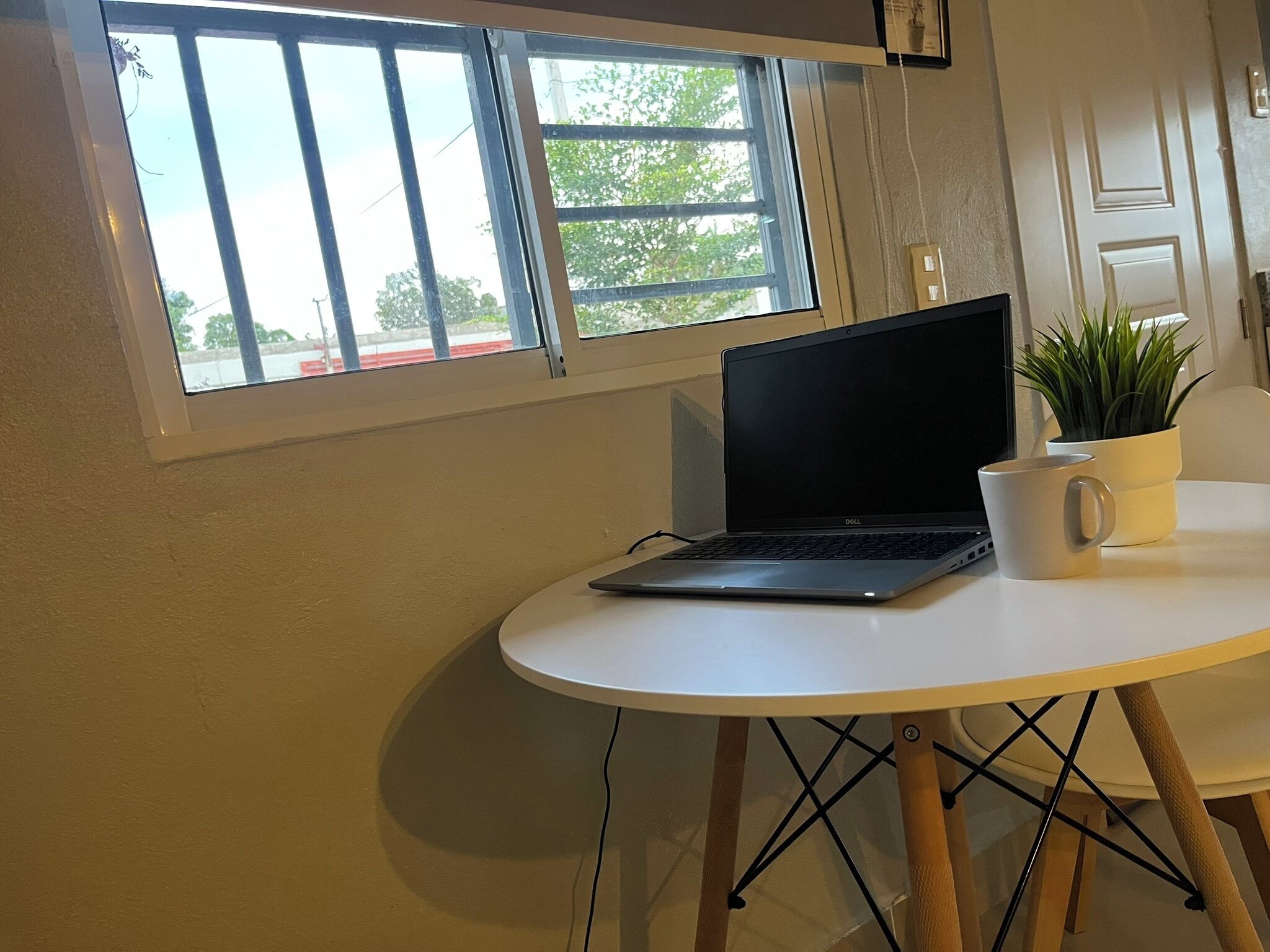 Een laptop op een witte tafel, met een potplant en een mok.