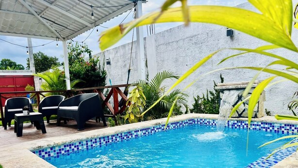 Una piscina amb mosaics blaus, envoltada per un porxo cobert amb cadires i una barbacoa.