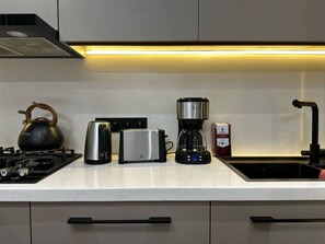 A kitchen with a gas stove, a kettle, a toaster, a coffee maker, and a sink. - Apartmenthotelsuz (Tashkent)