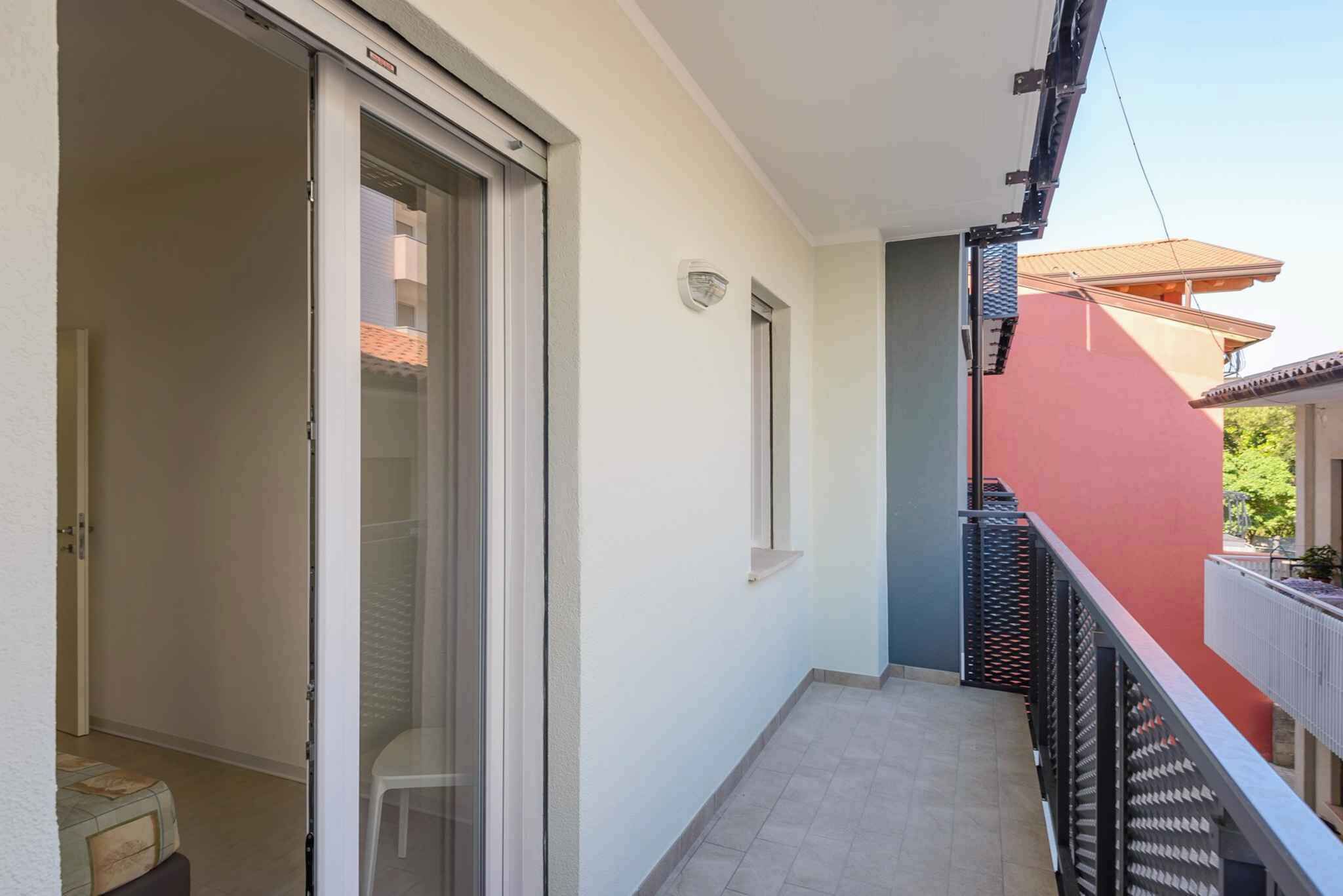 A narrow balcony with a sliding glass door leading to a room, a small window, and a red wall.