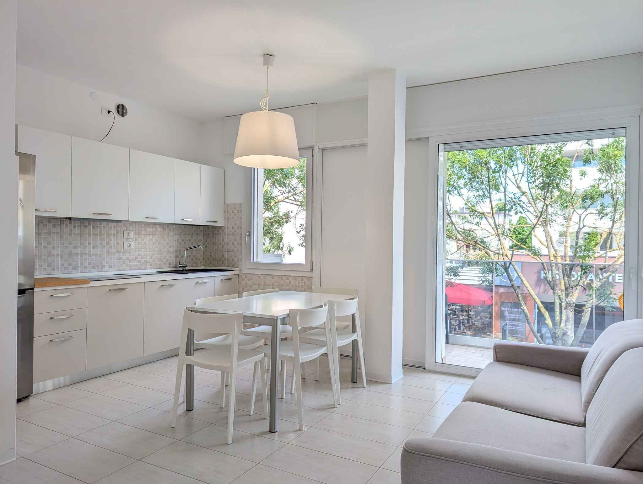 Een moderne keuken met witte kasten en een eethoek met een witte tafel en stoelen.