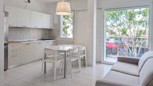 A modern kitchen with white cabinets and a dining area with a white table and chairs. - Holiday apartment with air conditioning and balcony (Lignano Sabbiadoro)