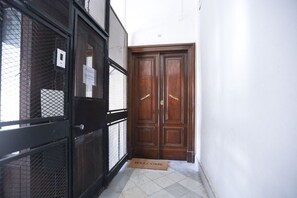 Un couloir avec un portail en métal noir, une porte double en bois et un paillasson.