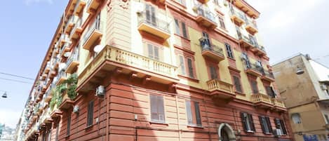 Un edificio de varios pisos con balcones, entrada a nivel de calle y coches aparcados.